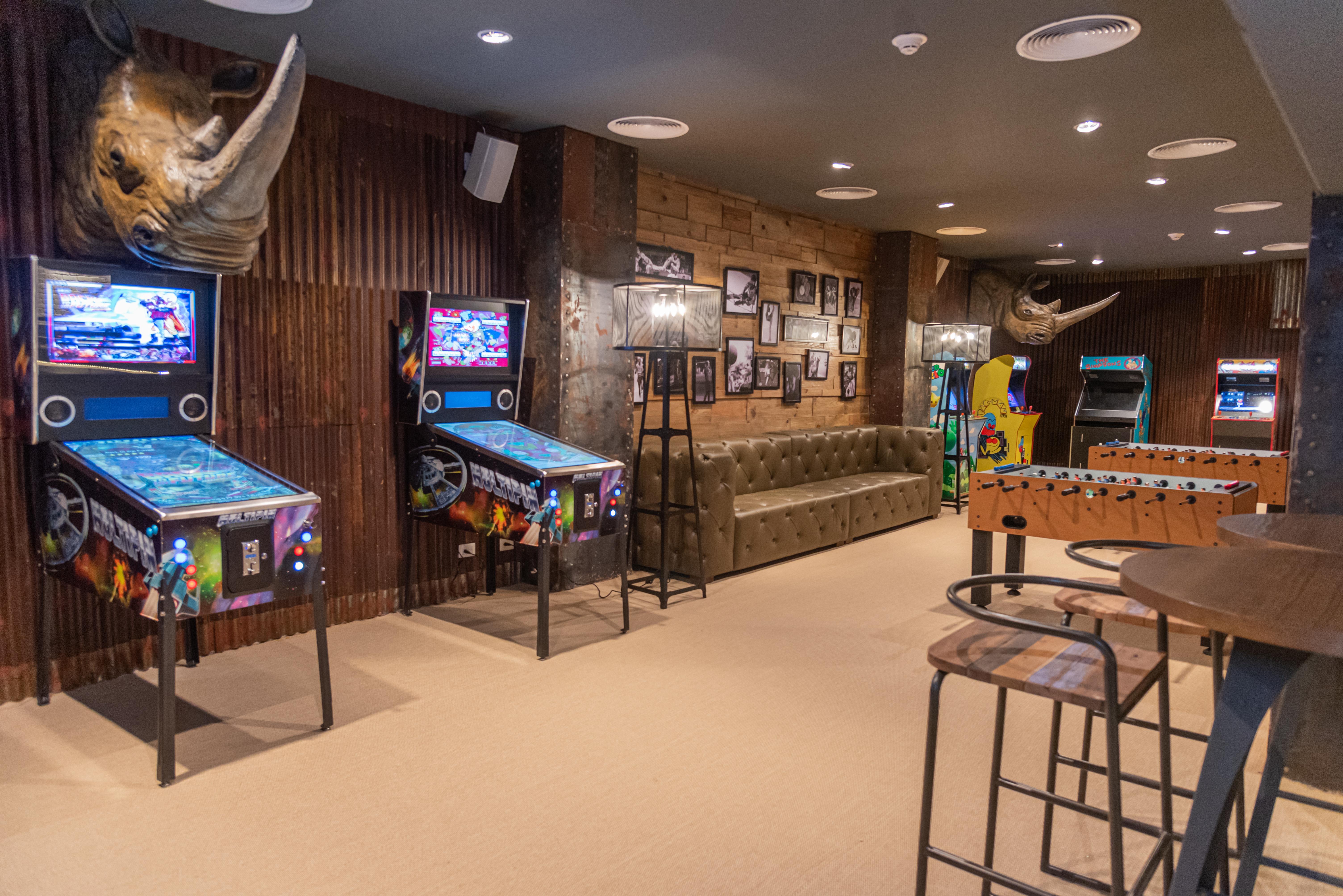 Grand Bavaro Princess (Adults Only) Zewnętrze zdjęcie The photo shows a game room with a cozy and fun atmosphere. On the left side, there are two pinball machines with colorful graphics. A tufted green sofa is situated against the wall, providing a comfortable seating area. The walls are decorated with 